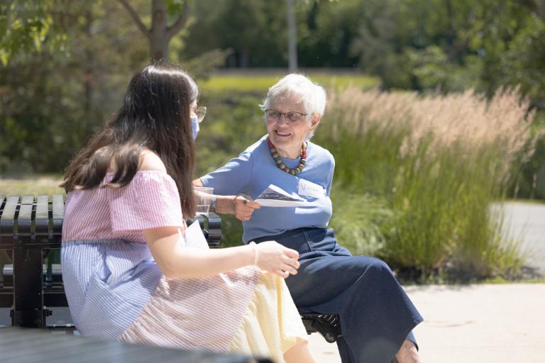 Photo of student and senior woman sitting on a bench and talking